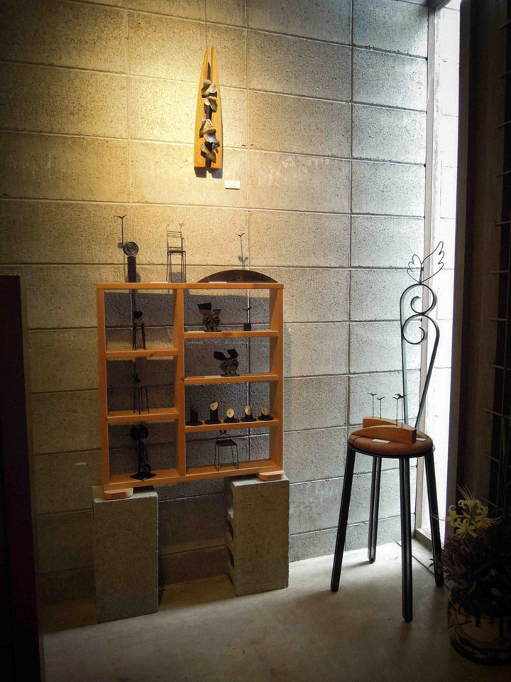 鉄で出来ている実際に座れる椅子のオブジェ。ユニークな背のデザイン。角を落とした木の座面が柔らかい印章を添えます。 コーナーに展示した様子の写真。