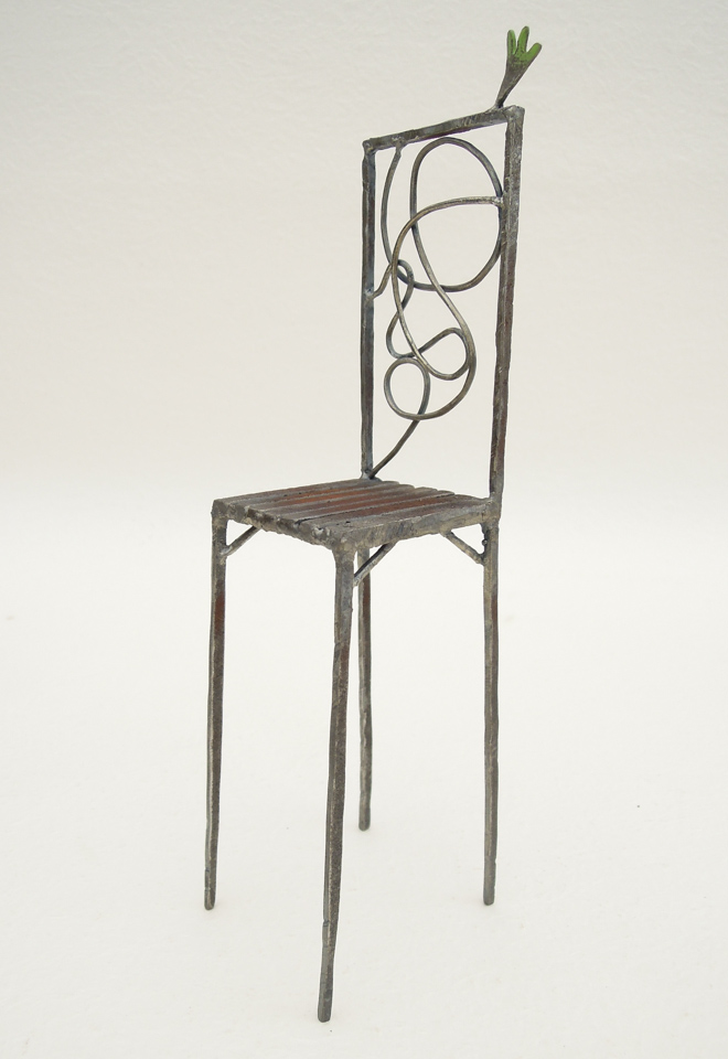 鉄で出来ている椅子のオブジェ。ユニークなハイバックデザイン。卓上サイズながら繊細に作りこまれたディテール。 トップに小さな翼が付いています。斜めからの写真。