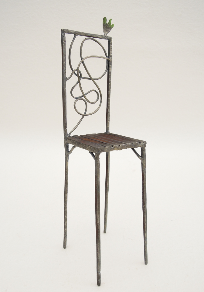 鉄で出来ている椅子のオブジェ。ユニークなハイバックデザイン。卓上サイズながら繊細に作りこまれたディテール。 トップに小さな翼が付いています。斜めからの写真。