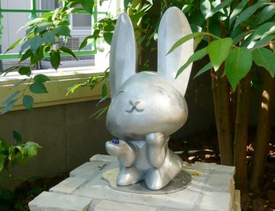 ウサギのアートオブジェの写真。ウサギは屋外設置でも耐久性のあるアルミ鋳造無垢です。レンガを積んだ台の上に設置されています。