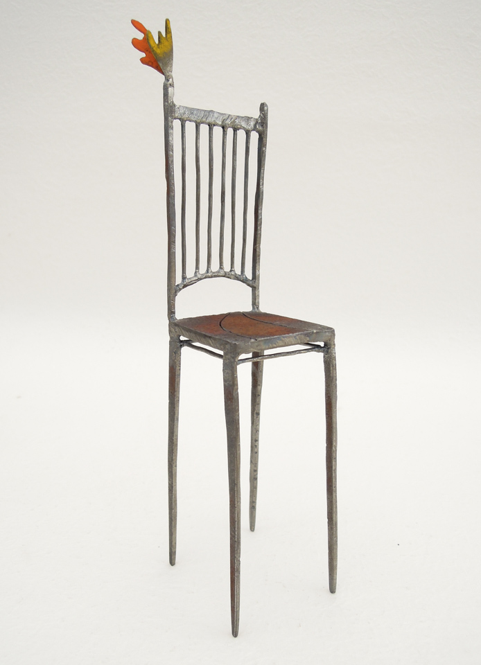 鉄で出来ている椅子のオブジェ。スタイリッシュなハイバックデザイン。卓上サイズながら繊細に作りこまれたディテール。トップに小さな翼が付いています。斜めからの写真。