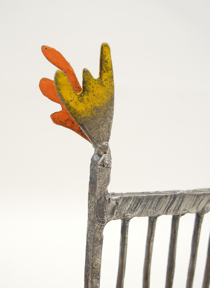 鉄で出来ている椅子のオブジェ。スタイリッシュなハイバックデザイン。卓上サイズながら繊細に作りこまれたディテール。トップ付いた小さな翼のアップ写真。2枚の羽が岩絵の具で着彩されています。