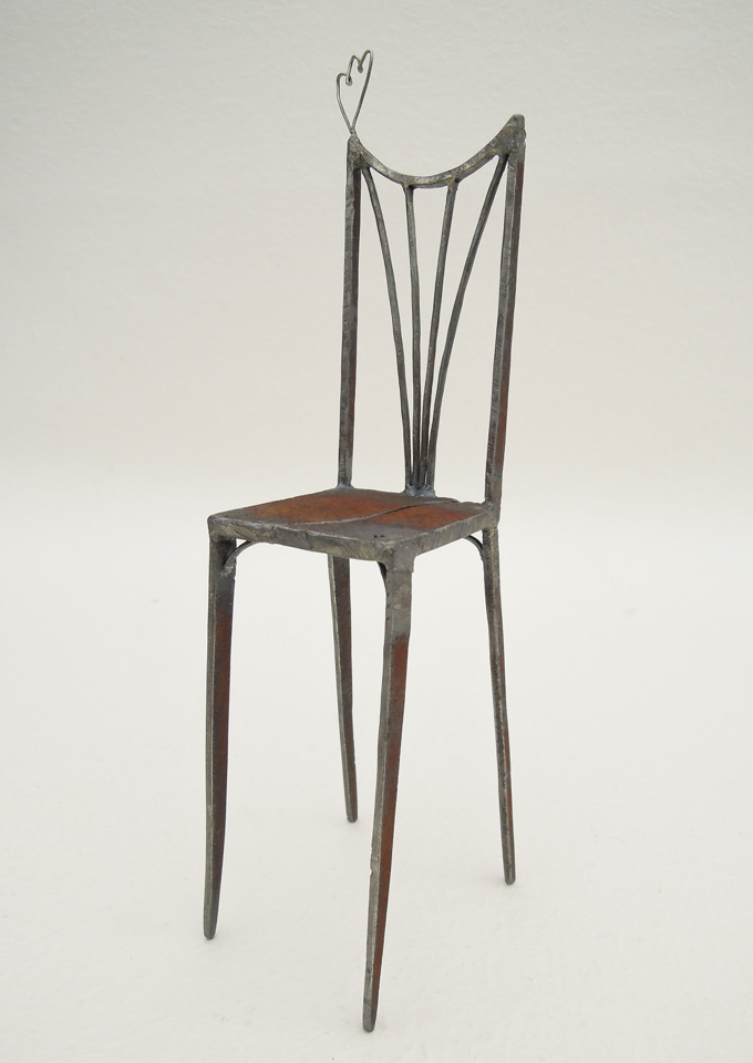 鉄で出来ている椅子のオブジェ。スタイリッシュなハイバックデザイン。卓上サイズながら繊細に作りこまれたディテール。トップに小さな翼が付いています。斜めからの写真。