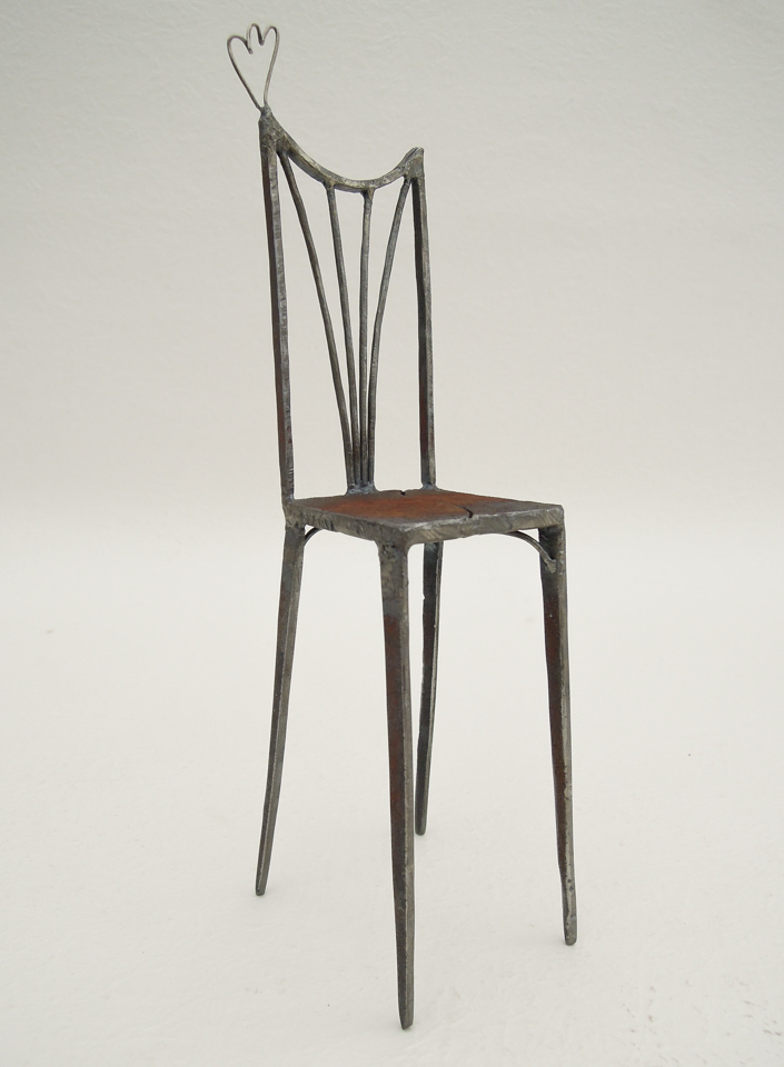 鉄で出来ている椅子のオブジェ。スタイリッシュなハイバックデザイン。卓上サイズながら繊細に作りこまれたディテール。トップに小さな翼が付いています。斜めからの写真。