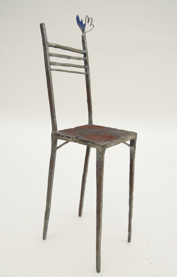 鉄で出来ている椅子のオブジェ。スタイリッシュなハイバックデザイン。卓上サイズながら繊細に作りこまれたディテール。トップに小さな翼が付いています。斜めからの写真。