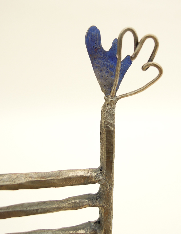 鉄で出来ている椅子のオブジェ。スタイリッシュなハイバックデザイン。卓上サイズながら繊細に作りこまれたディテール。トップ付いた小さな翼のアップ写真。岩絵の具で青く着彩したソリッドの翼と、とても細い鉄線を鍛造したもので作った翼の組み合わせです。