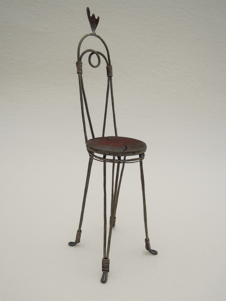 鉄で出来ている椅子のオブジェ。スタイリッシュなハイバックデザイン。卓上サイズながら繊細に作りこまれたディテール。トップに小さな翼が付いています。斜めからの写真。