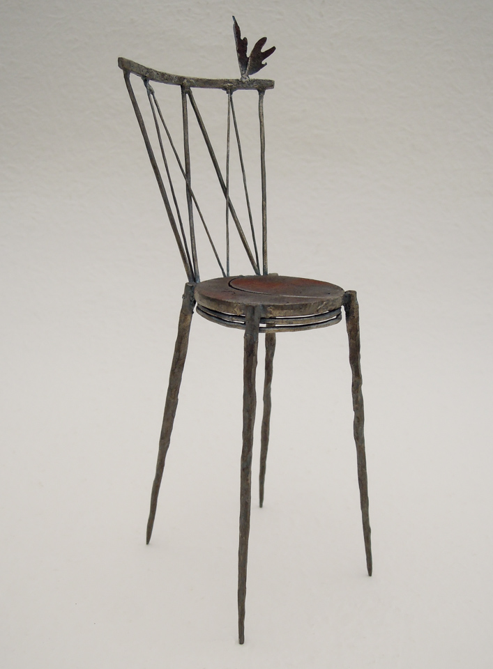 鉄で出来ている椅子のオブジェ。スタイリッシュなハイバックデザイン。卓上サイズながら繊細に作りこまれたディテール。トップに小さな翼が付いています。斜めからの写真。