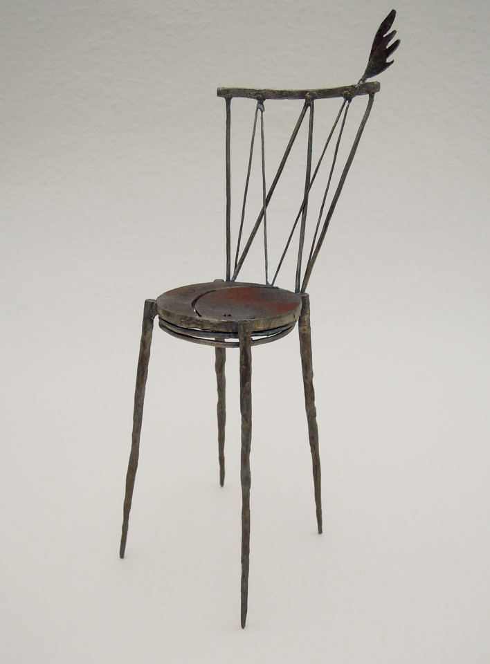 鉄で出来ている椅子のオブジェ。スタイリッシュなハイバックデザイン。卓上サイズながら繊細に作りこまれたディテール。トップに小さな翼が付いています。斜めからの写真。