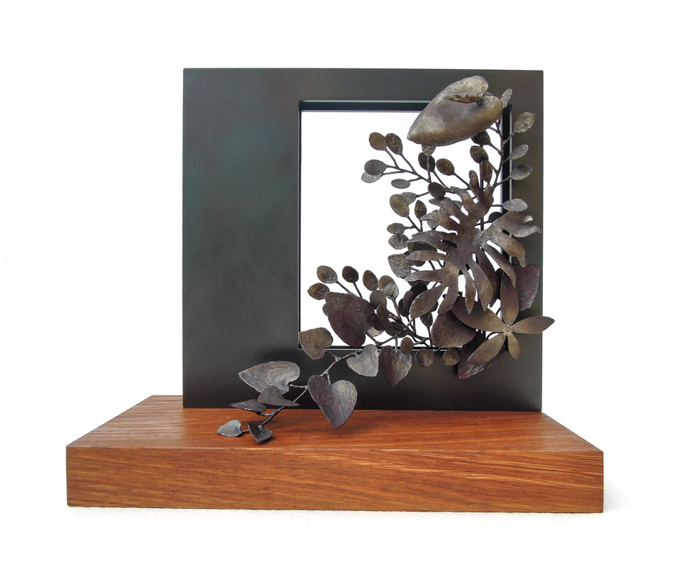 四角い窓から様々な植物が溢れでているようなアートオブジェです。窓と植物は鉄、ベースは木でできています。正面写真。