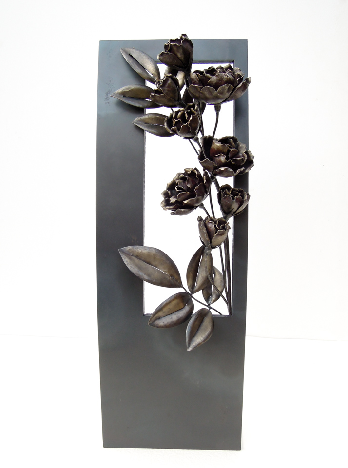 縦長の窓から一枝のバラが咲き誇っているアートオブジェです。窓はゆるやかな曲面になっており、花付きの良い枝がいきいきと伸びています。フレーム、バラともに鉄で制作し、同じ素材で色味の違いを出しています。正面写真。