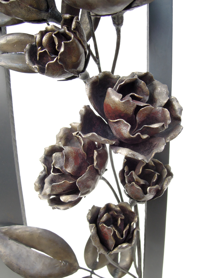 縦長の窓から一枝のバラが咲き誇っている鉄のアートオブジェです。花のアップ写真。