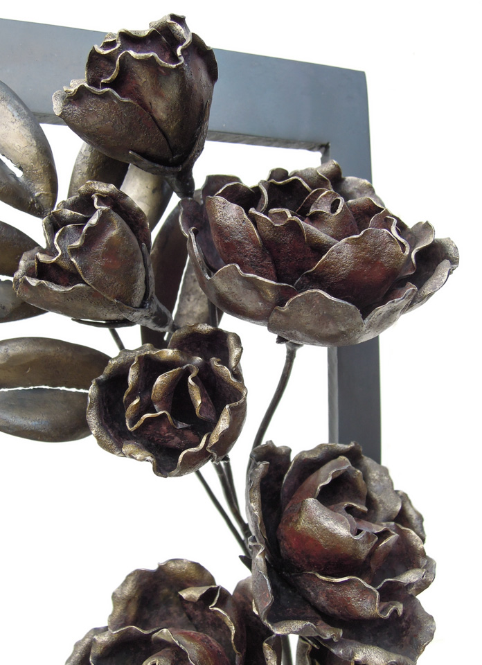 縦長の窓から一枝のバラが咲き誇っている鉄のアートオブジェです。花のアップ写真。