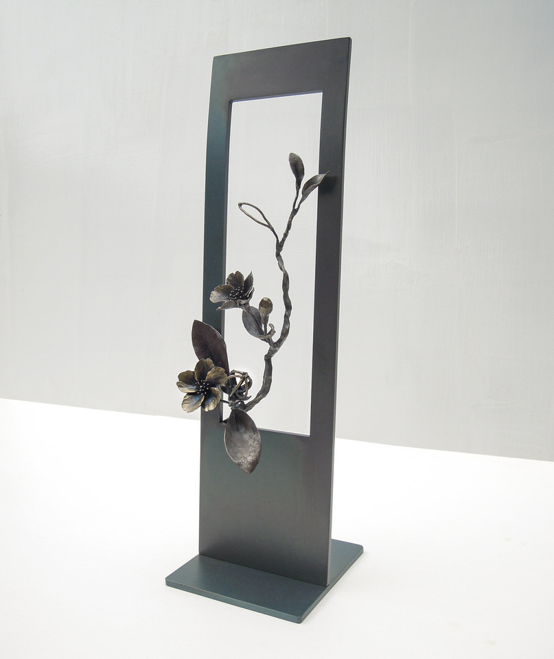 縦長のプレートに開いた窓からひと枝の山桜がのぞいている様子を鉄で表現したアート作品です。実際の桜の花と同じ大きさです。