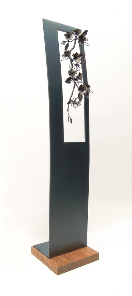 青みを残して黒焼きした鉄のプレートの窓から、鍛鉄の桜の枝が下がっている姿のアート作品です。斜めからの写真。