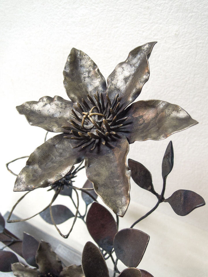 弓状の鉄プレートに鍛鉄のクレマチスの花が添えられたアート作品です。花の表現。