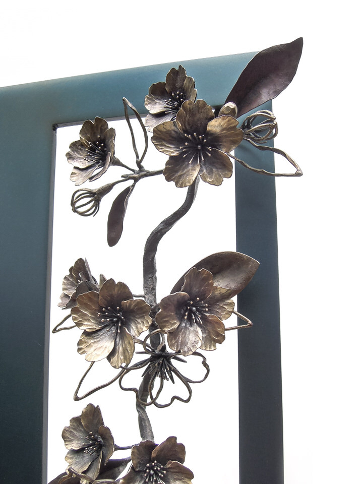 青みを残して黒焼きした鉄のプレートの窓から、鍛鉄の桜の枝が下がっている姿のアート作品です。花の様子。