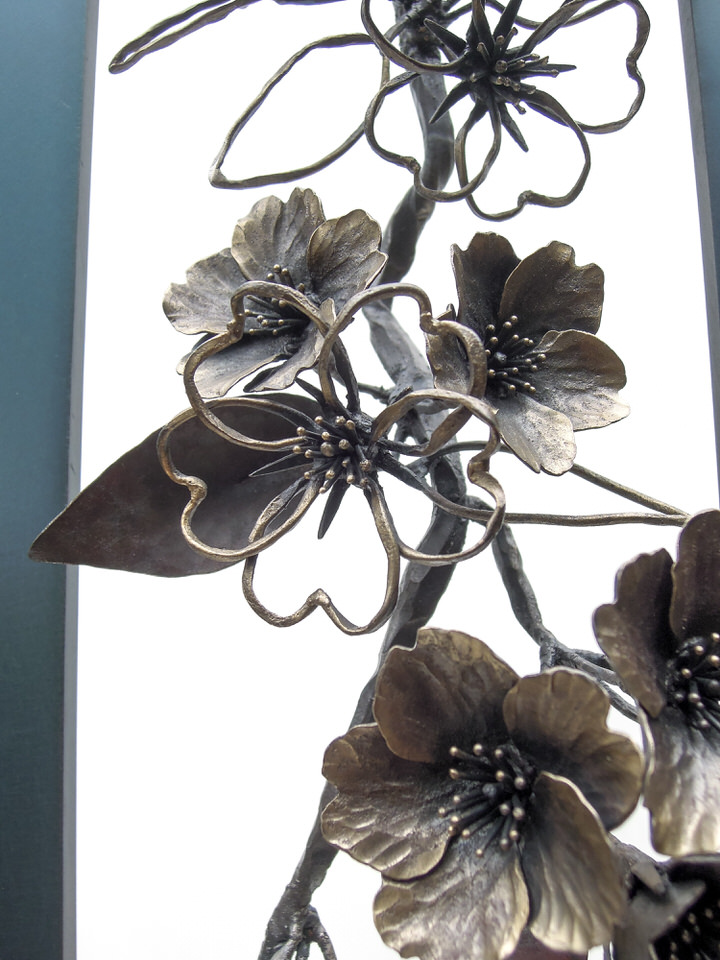 青みを残して黒焼きした鉄のプレートの窓から、鍛鉄の桜の枝が下がっている姿のアート作品です。花の様子。