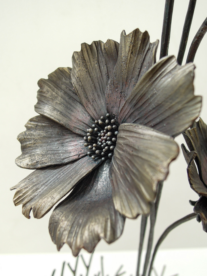 円の鉄プレートに鍛鉄のコスモスの花が添えられた彫刻作品です。咲いたばかりのコスモスの花。花弁にはハリがあり、花芯は中心部が窪んでいます。