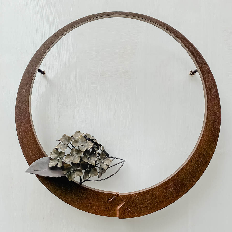 紫陽花のこんもりした花が円の中に添えられているアート作品、鉄の彫刻です。 柔らかい花びらを模した鉄のアジサイの花に、面と線で表現した葉が寄り添っています。 壁面に取り付けるタイプです。