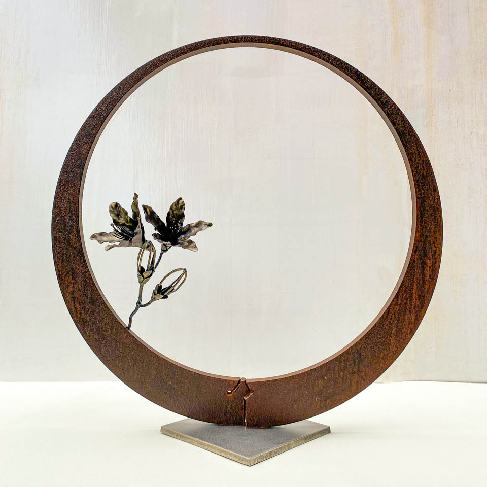 箱根の春を彩るミツバツツジの花を円弧に添えた鉄の彫刻、アート作品です。スタンドタイプです。蕾は鍛造した鉄線で表現し軽い印象になっています。円弧は厚みのある鉄を切り出し、下部でズラして表情をつけています
